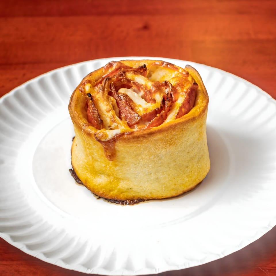 A golden-brown Villa Formia pizza roll, filled with cheese and pepperoni, on a white plate.