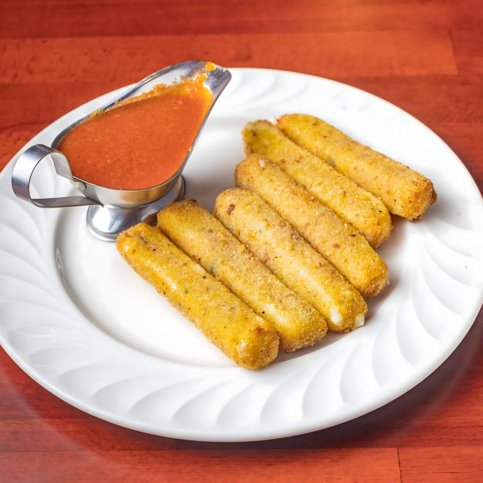 Golden-brown mozzarella sticks with a side of red marinara sauce in a silver gravy boat.