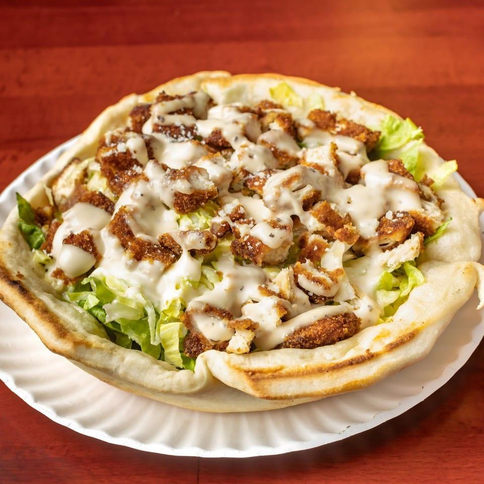 A Villa Formia pizza bowl filled with lettuce, crispy chicken, and creamy dressing on a white plate.