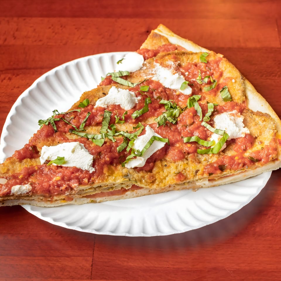 A thick slice of Villa Formia's pizza with red sauce, ricotta, and basil on a white plate.