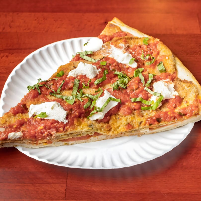 A thick slice of Villa Formia's pizza with red sauce, ricotta, and basil on a white plate.