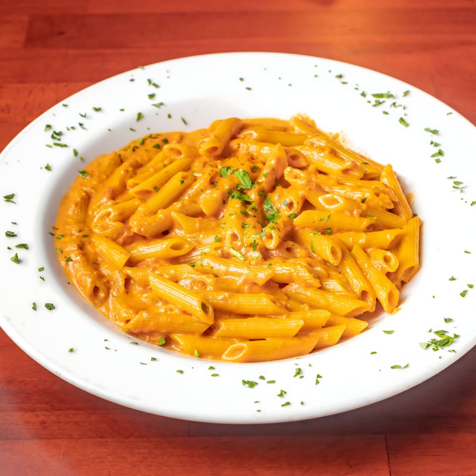 Penne pasta in a creamy orange sauce, garnished with fresh parsley, served in a white bowl.