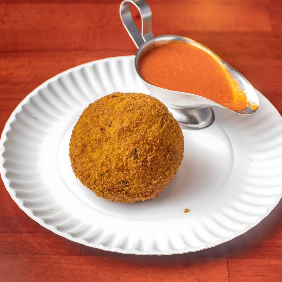 Golden-brown arancini on a white plate with a silver gravy boat of red marinara sauce.